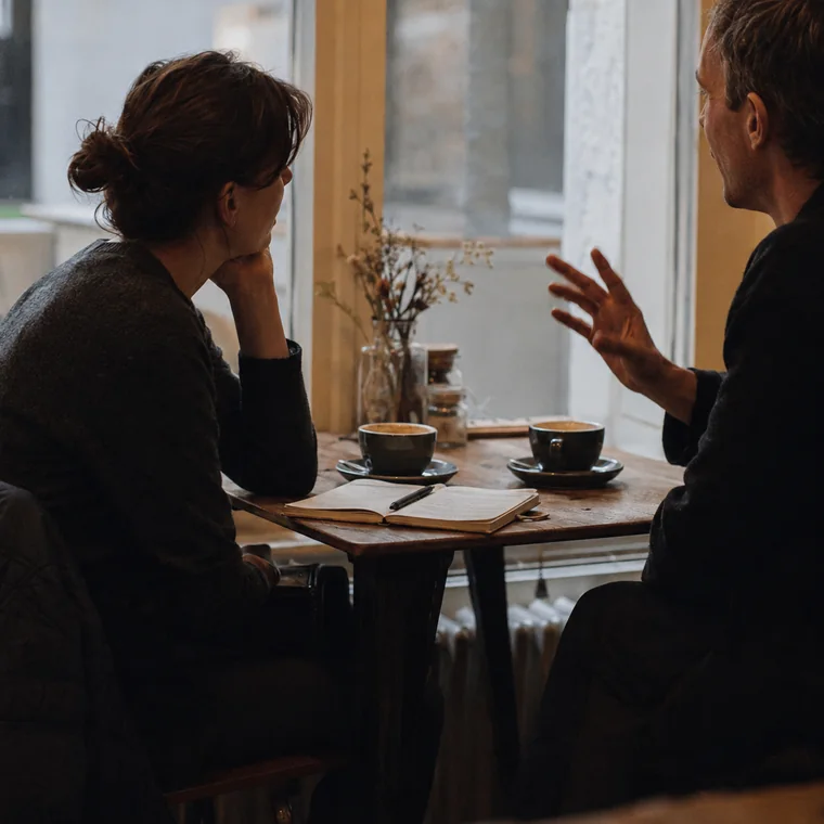 Dos personas conversando en una mesa, con un cuaderno abierto